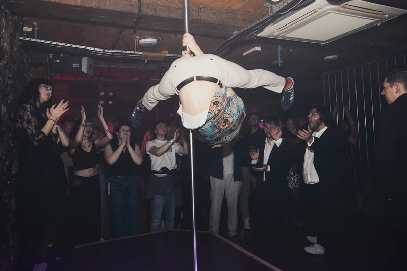 A man high up on a dancing pole surrounded by applauding crowds at OMG Plymouth